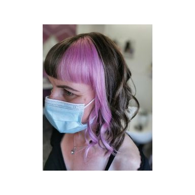 Person with shoulder-length hair featuring pink highlights, wearing a blue face mask.