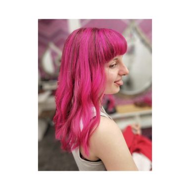 Young woman with long, wavy pink hair, turned slightly to the side.