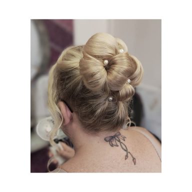 Blonde hair styled in an elegant updo with pearls, featuring a tattoo on the back.