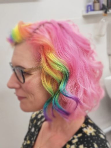 Profile of a woman with vibrant, multi-coloured hair and glasses, wearing a floral top.