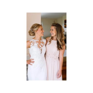 Two women smiling at each other, one in a bridal gown and the other in a pink dress.
