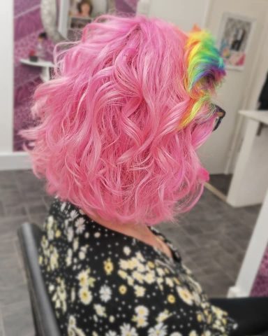 Curly pink hair with a rainbow accent, styled in a modern, vibrant look.